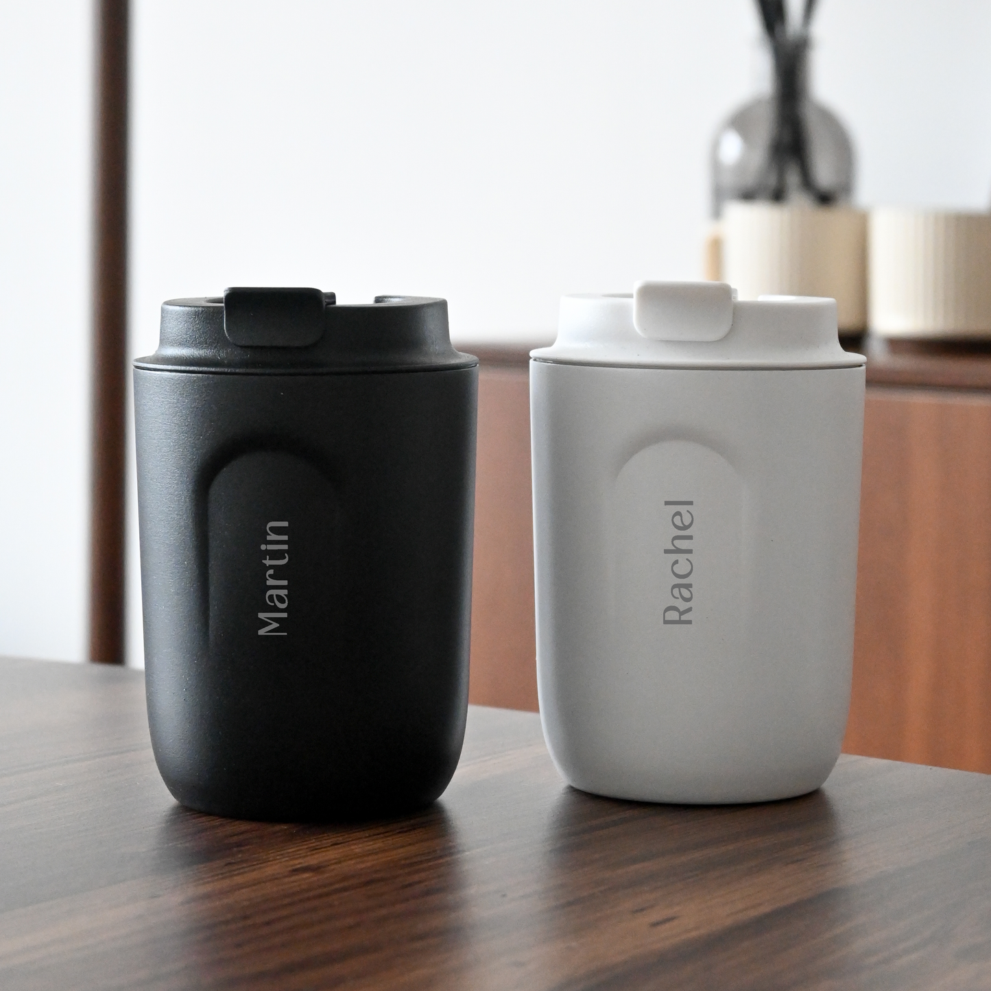Two insulated travel mugs, one black and one white, with names engraved on them Singapore