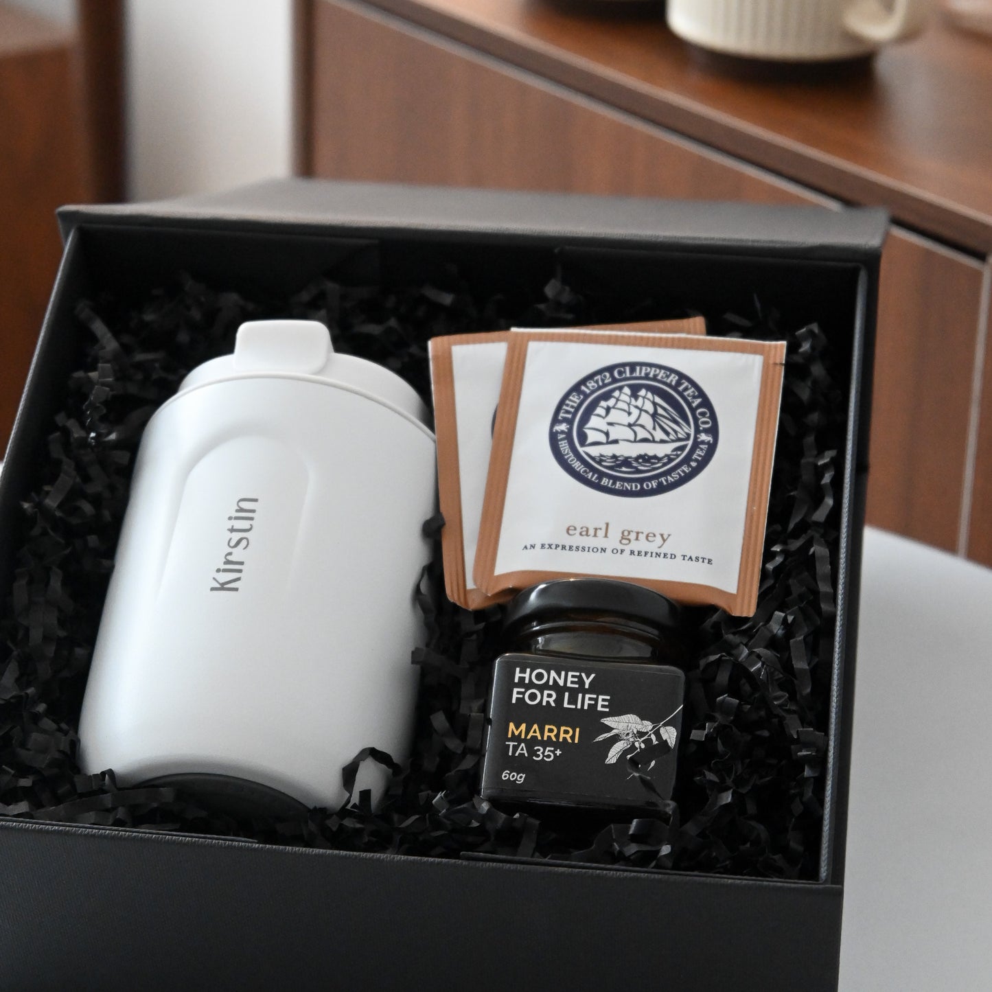 Gift set with a white personalised tumbler, tea bags, and honey in a black box
