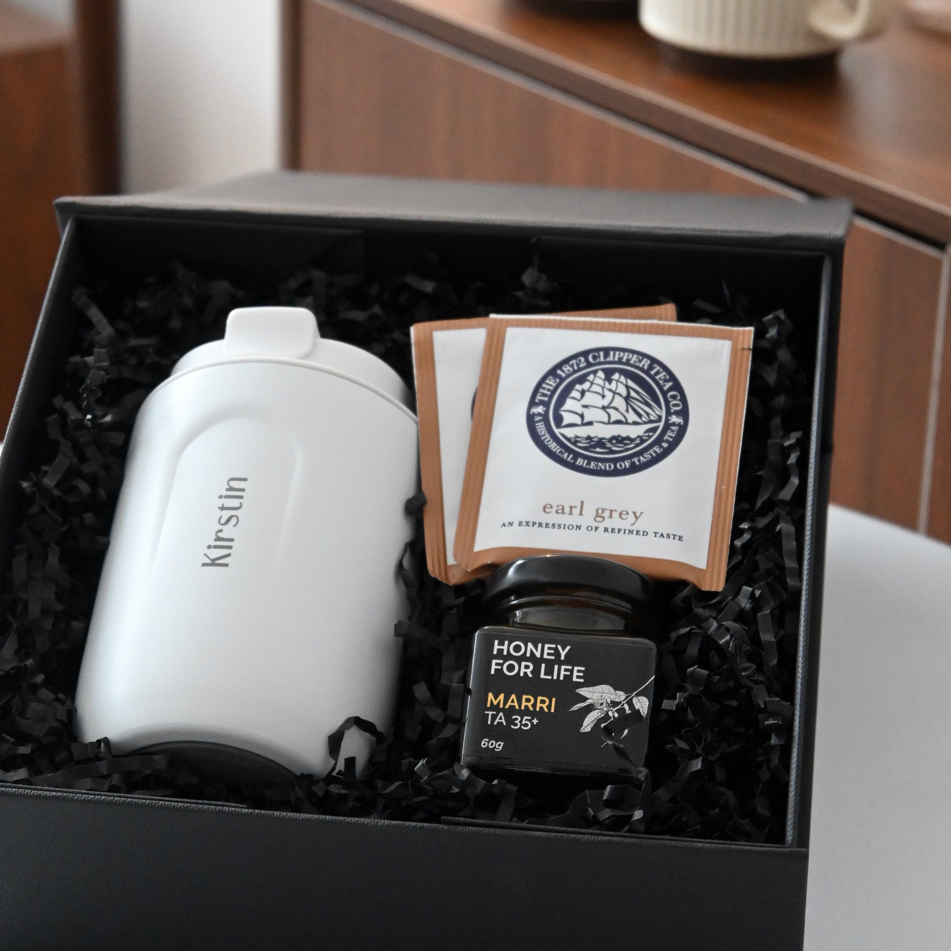 Gift set with a white personalised tumbler, tea bags, and honey in a black box